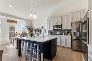 Kitchen with a sink, light countertops, light wood-style floors, appliances with stainless steel finishes, and tasteful backsplash