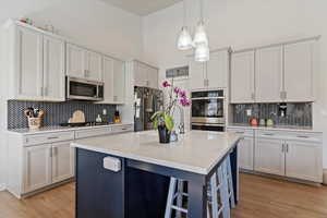 Kitchen featuring backsplash, decorative light fixtures, a center island with sink, light wood-type flooring, and stainless steel appliances