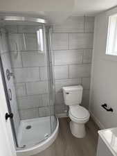 Full bath with toilet, baseboards, wood finished floors, and a stall shower