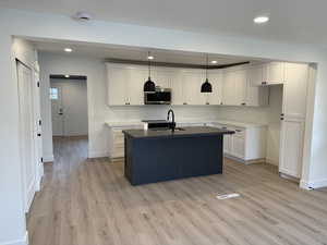 Kitchen with baseboards, recessed lighting, stainless steel microwave, a sink, and light wood-style flooring