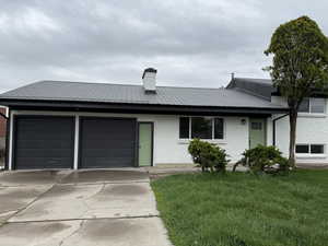 Ranch-style house featuring a garage, a front yard, metal roof, a chimney, and concrete driveway