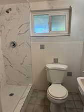 Bathroom with wainscoting, toilet, tile walls, walk in shower, and tile patterned floors