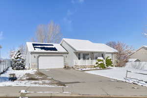 Ranch-style house featuring fence, driveway, a porch, a garage, and roof mounted solar panels