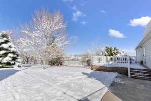 Yard covered in snow featuring a deck and fence