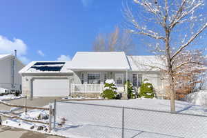 Ranch-style house featuring a fenced front yard, roof mounted solar panels, covered porch, and driveway