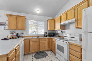 Kitchen with under cabinet range hood, light floors, light countertops, white appliances, and a sink