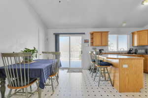 Kitchen featuring light floors, a breakfast bar, vaulted ceiling, a peninsula, and open shelves