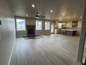 Unfurnished living room featuring light wood finished floors, baseboards, ceiling fan, recessed lighting, and a textured ceiling
