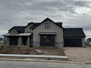 View of front facade with stone siding, an attached garage, driveway, and board and batten siding