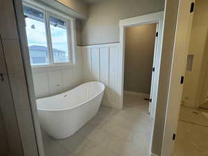 Bathroom with tile patterned floors, a wainscoted wall, a freestanding bath, and a decorative wall
