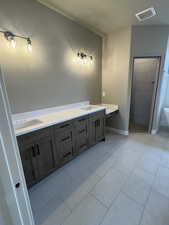 Bathroom with tile patterned flooring, visible vents, baseboards, tiled shower, and a sink