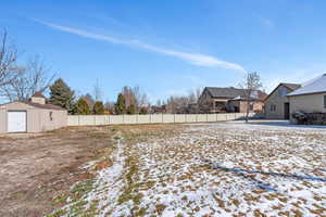 Yard covered in snow featuring an outbuilding, a residential view, and fence