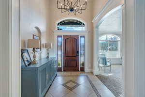 Foyer featuring light tile patterned floors, baseboards, arched walkways, and an inviting chandelier