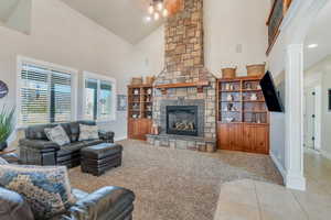 Carpeted living room featuring tile patterned floors, high vaulted ceiling, a stone fireplace, baseboards, and ornate columns