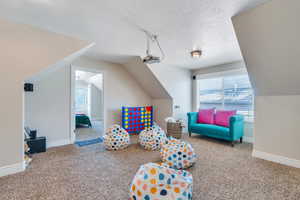 Rec room featuring baseboards, carpet floors, a textured ceiling, and vaulted ceiling