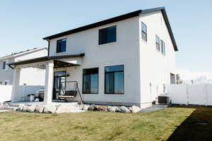 Rear view of house featuring stucco siding, covered patio, rock retaining wall, lawn, garden space, and fence.