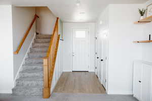 Entryway featuring stairway, accent wall, half bath, coat closet, and wood-finished floors