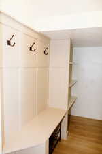 Updated mudroom with coat hooks, shoe rack, shelving, under-the-stairs storage, and light wood-style flooring