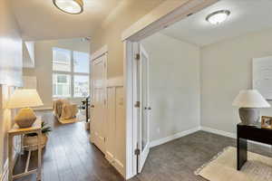 Corridor with dark wood-style floors, lofted ceiling, and baseboards