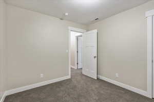 Unfurnished bedroom with dark colored carpet, visible vents, baseboards, and a textured ceiling