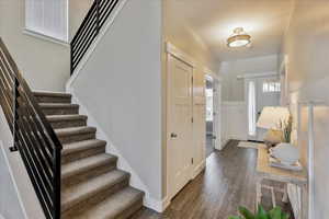 Entryway featuring a wainscoted wall, stairway, and dark wood-style flooring