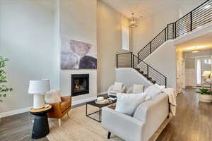Living room with hardwood / wood-style floors, stairway, baseboards, a towering ceiling, and a glass covered fireplace