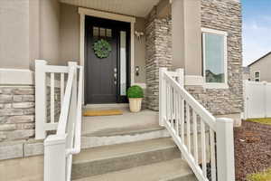 Entrance to property with stone siding, stucco siding, and fence