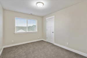 Spare room featuring visible vents, carpet, baseboards, and a textured ceiling