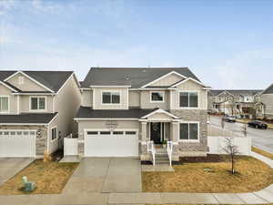 View of front of home with stone siding, fence, board and batten siding, concrete driveway, and a garage