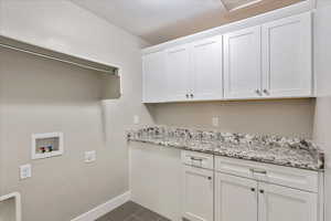 Laundry area with washer hookup, dark tile patterned floors, a textured ceiling, cabinet space, and baseboards