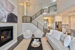 Living room with baseboards, stairs, dark wood-type flooring, a towering ceiling, and a glass covered fireplace