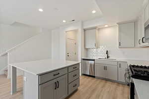 Kitchen featuring light wood finished floors, gray cabinetry, a sink, stainless steel appliances, and light countertops