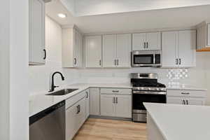 Kitchen with backsplash, light wood-type flooring, light countertops, stainless steel appliances, and a sink