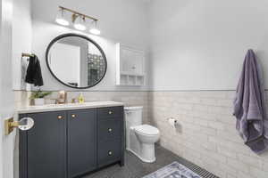 Bathroom featuring vanity, a wainscoted wall, tile patterned flooring, tile walls, and toilet