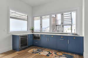 Kitchen with blue cabinetry, baseboards, beverage cooler, light countertops, and wood finished floors