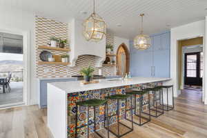 Kitchen featuring open shelves, a sink, decorative backsplash, light countertops, and light wood-style floors
