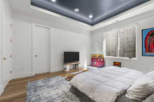 Bedroom featuring recessed lighting, baseboards, a tray ceiling, and wood finished floors