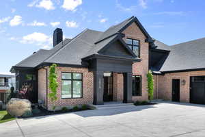 View of front of home with brick siding, roof with shingles, and a chimney