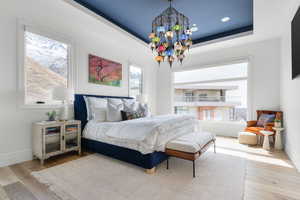 Bedroom with baseboards, a raised ceiling, a notable chandelier, and wood finished floors