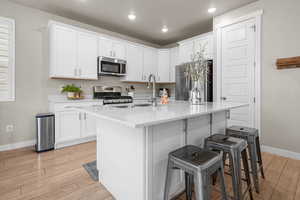 Kitchen with a breakfast bar, stainless steel appliances, light countertops, white cabinets, and light wood-type flooring
