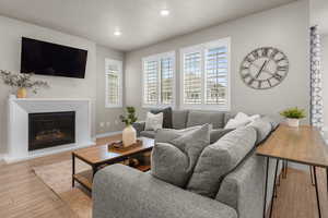 Living room with a glass covered fireplace, hardwood / wood-style flooring, recessed lighting, and a textured ceiling