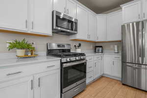 Kitchen featuring light wood-style floors, appliances with stainless steel finishes, white cabinets, and light countertops