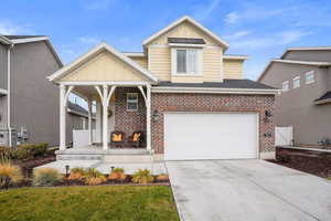 View of front facade featuring driveway, a porch, board and batten siding, a garage, and brick siding