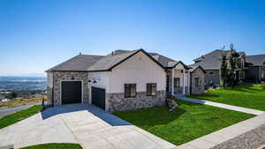 View of front of property with a front lawn, stone siding, board and batten siding, concrete driveway, and an attached garage