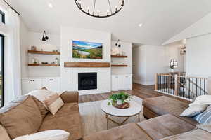 Living room featuring a brick fireplace, baseboards, vaulted ceiling, an inviting chandelier, and wood finished floors