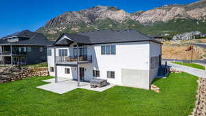 Rear view of house featuring a patio, a balcony, a yard, and a mountain view