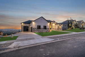 Modern inspired farmhouse featuring driveway, stone siding, board and batten siding, an attached garage, and a front yard