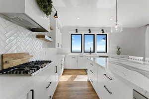 Kitchen with tasteful backsplash, stainless steel gas cooktop, light wood-type flooring, custom range hood, and white cabinets