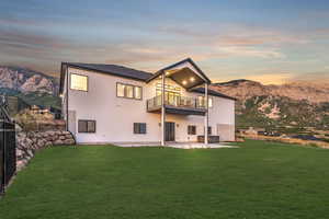Rear view of property featuring stucco siding, a lawn, a patio, a mountain view, and a balcony