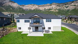 Back of house featuring a lawn, fence, a mountain view, a balcony, and a patio area
